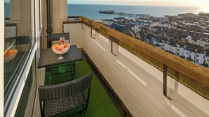 Ein Balkon mit Tisch und Stühlen, Blick auf das Meer und eine Stadt, sowie ein Schiff in der Ferne.