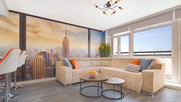 Ein modernes Wohnzimmer mit einem großen Fenster, einem beigefarbenen Sofa, einem runden Couchtisch und einer Wandmalerei mit Stadtansicht.