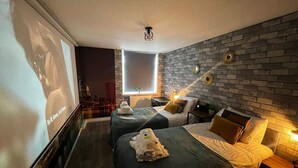 A hotel room with two beds, a large screen, a brick wall, and a cityscape view. - Central Brighton 1-bedroom Flat Modern & Bright Walk to Beach Sleeps 2 (Brighton)