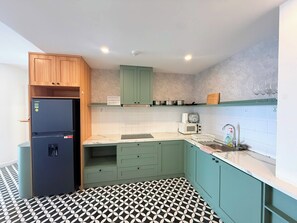 Een kleine keuken met een koelkast, magnetron, spoelbak en kastjes.