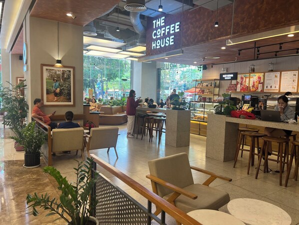 A coffee shop interior with seating areas, a counter with a menu, and a large window providing a view of the outdoors. - Apartment Lotte (Nha Trang)