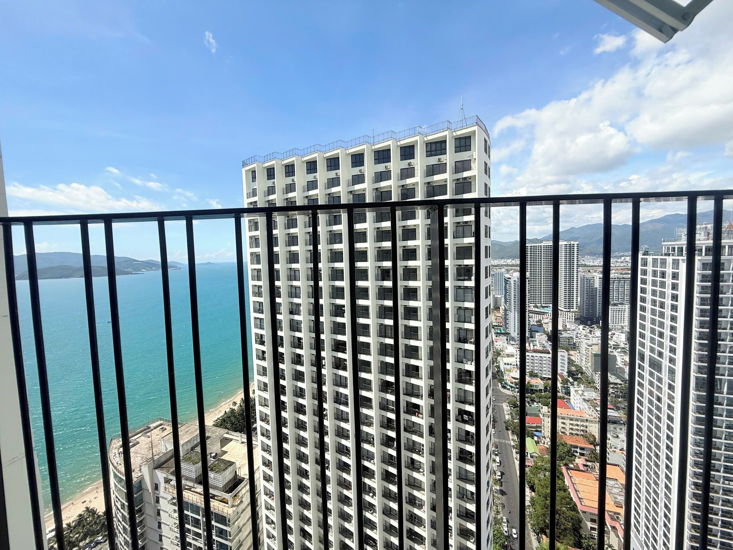 Um edifício alto com vários andares, guarda-corpo de varanda e vista para o mar e outros edifícios.