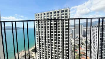 Um edifício alto com vários andares, guarda-corpo de varanda e vista para o mar e outros edifícios.