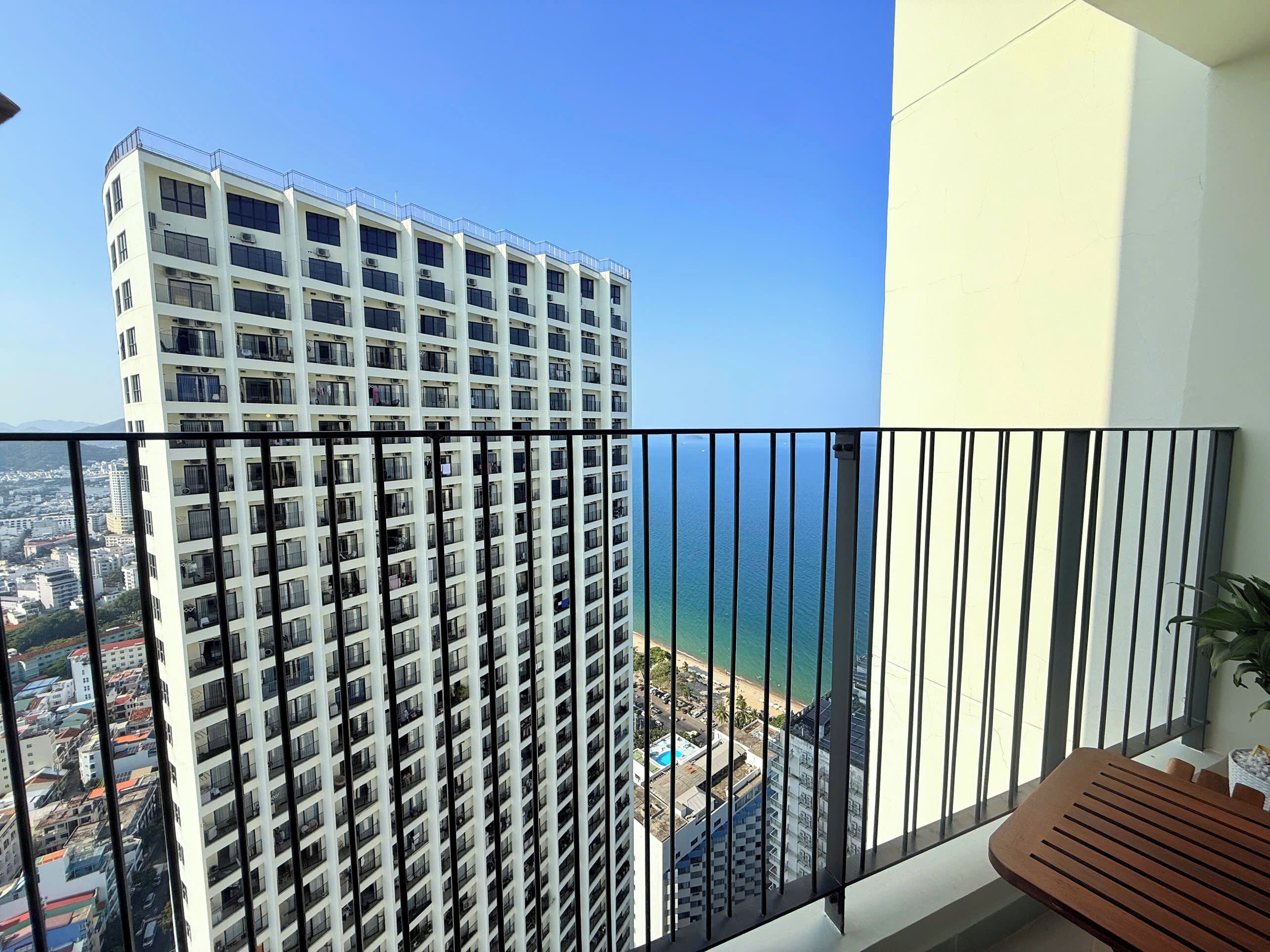 A high-rise building with multiple balconies, a clear view of the ocean, and a balcony with a wooden table.