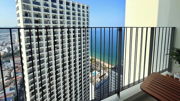 A high-rise building with multiple balconies, a clear view of the ocean, and a balcony with a wooden table.