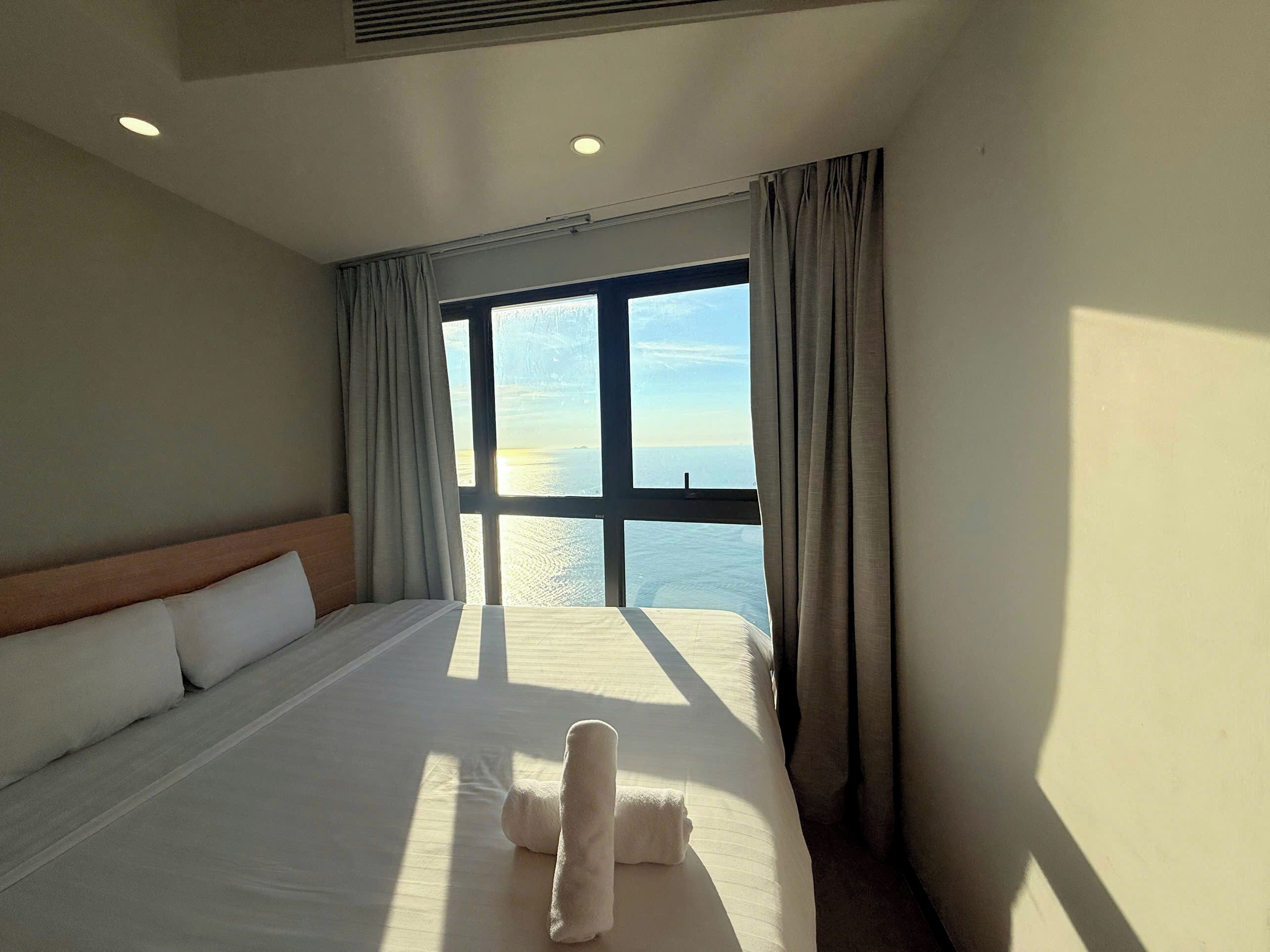 A hotel room with a large bed, a headboard, and a view of the sea through a window.