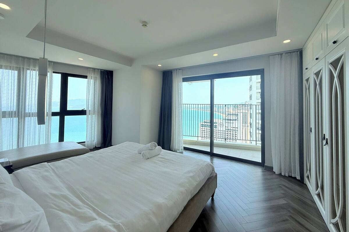 A modern hotel room with a large bed, a balcony with a city view, and a wardrobe.