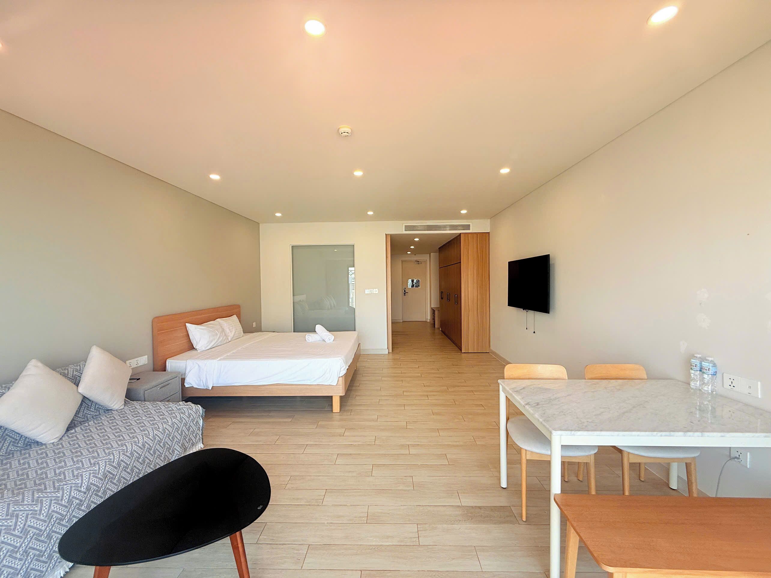 Quarto de hotel com uma cama, uma escrivaninha, uma cadeira e uma televisão.