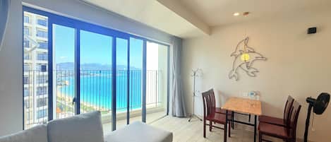 A modern living room with a sofa, dining table, chairs, and a view of the sea.