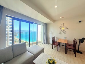 A modern living room with a sofa, dining table, chairs, and a view of the sea.