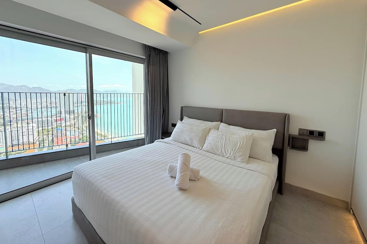 A modern hotel room with a large bed, a view of the cityscape, and a balcony with a railing.