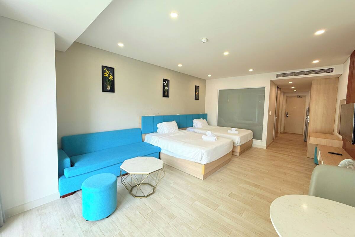 A modern hotel room with two beds, a blue sofa, a small round table, and a large mirror.