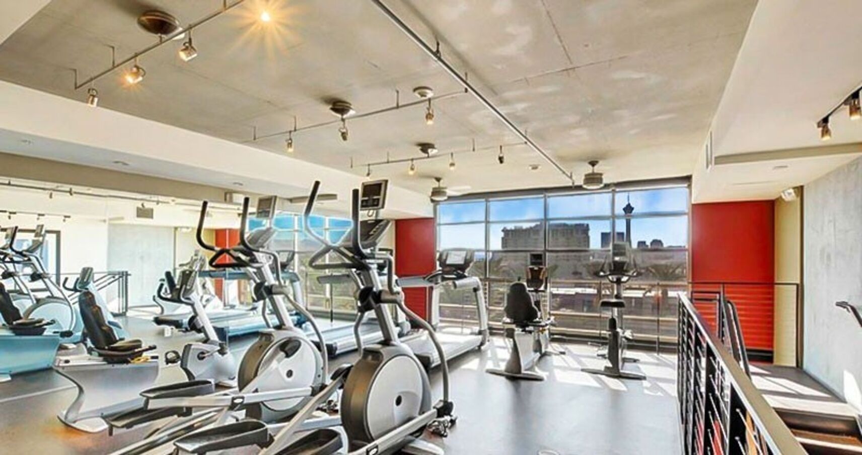 A gym with various exercise machines, large windows, and a view of the city.
