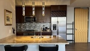 Une cuisine moderne dotée d’un îlot central, d’appareils électroménagers en acier inoxydable et de luminaires suspendus.