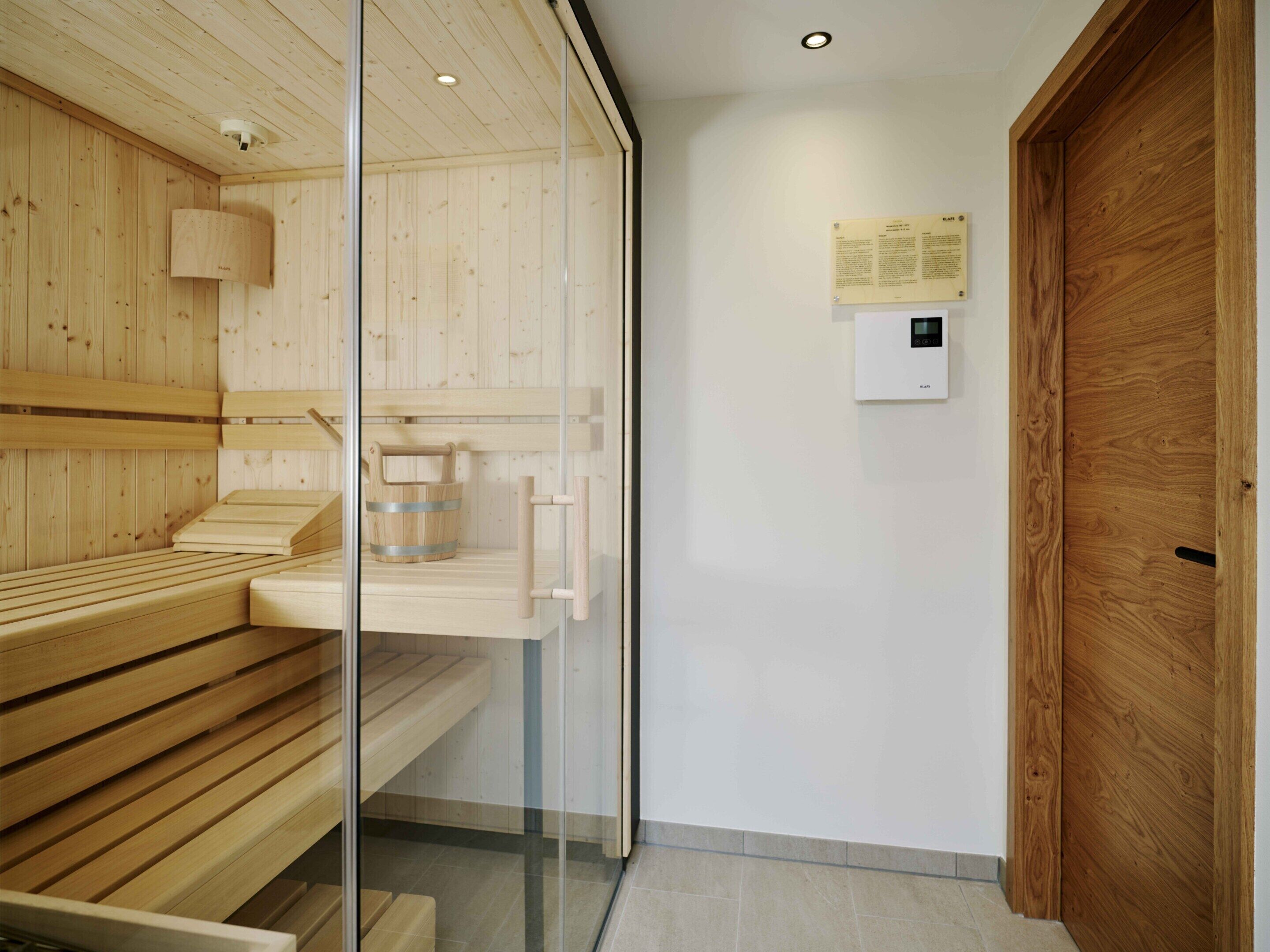 A modern sauna room with wooden benches, a glass partition, and a wooden door.