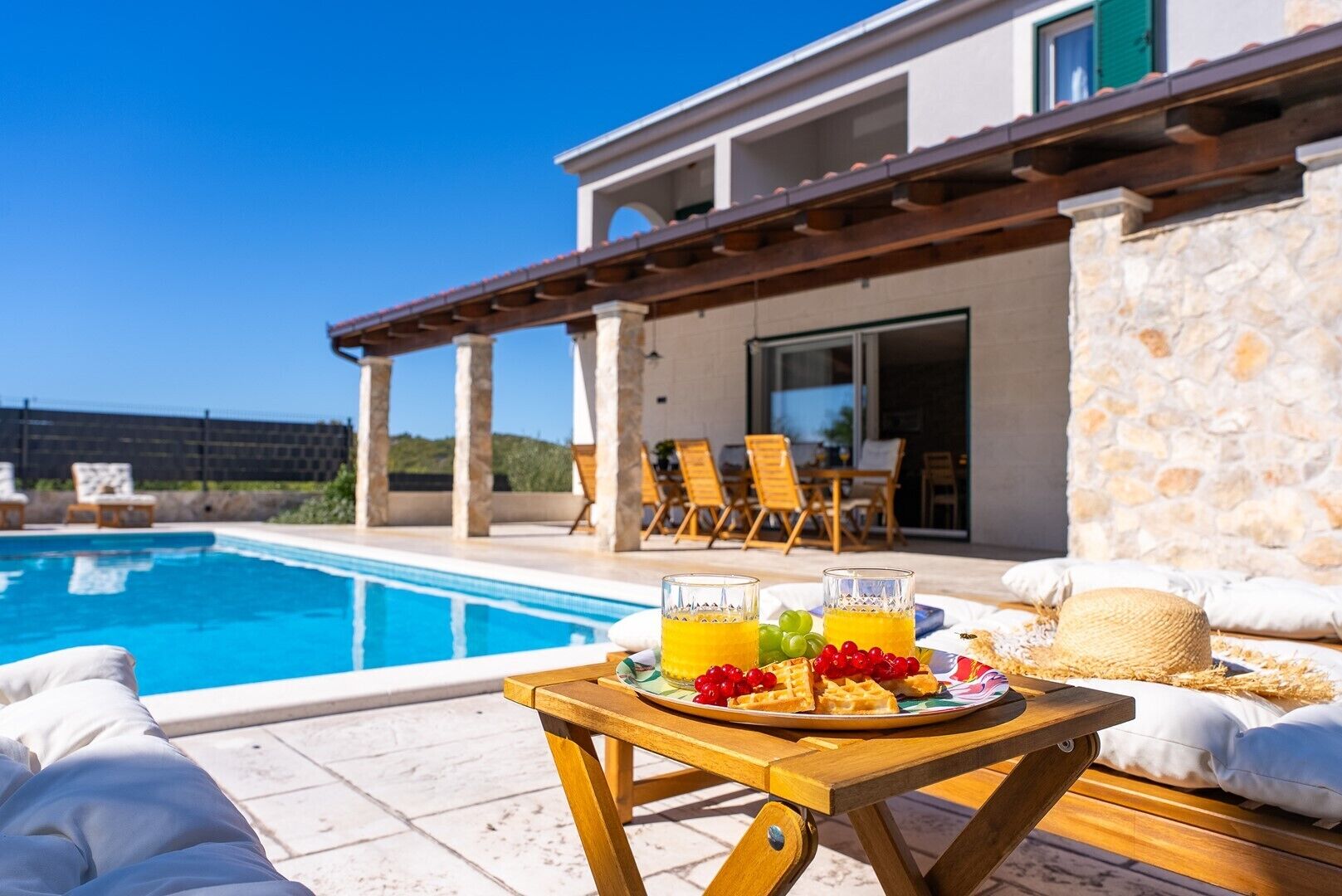 A poolside breakfast setup with a table, chairs, and a view of the pool and building.