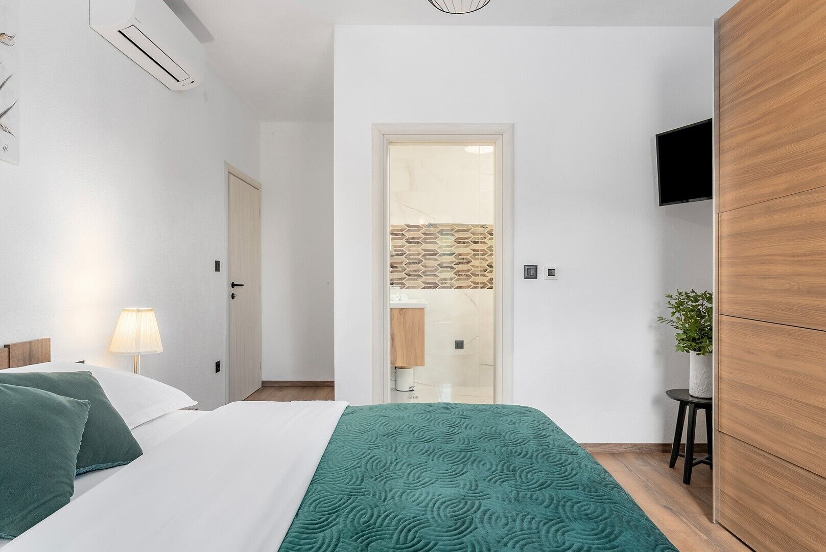 A bedroom with a bed, bedside lamp, and a TV on the wall.