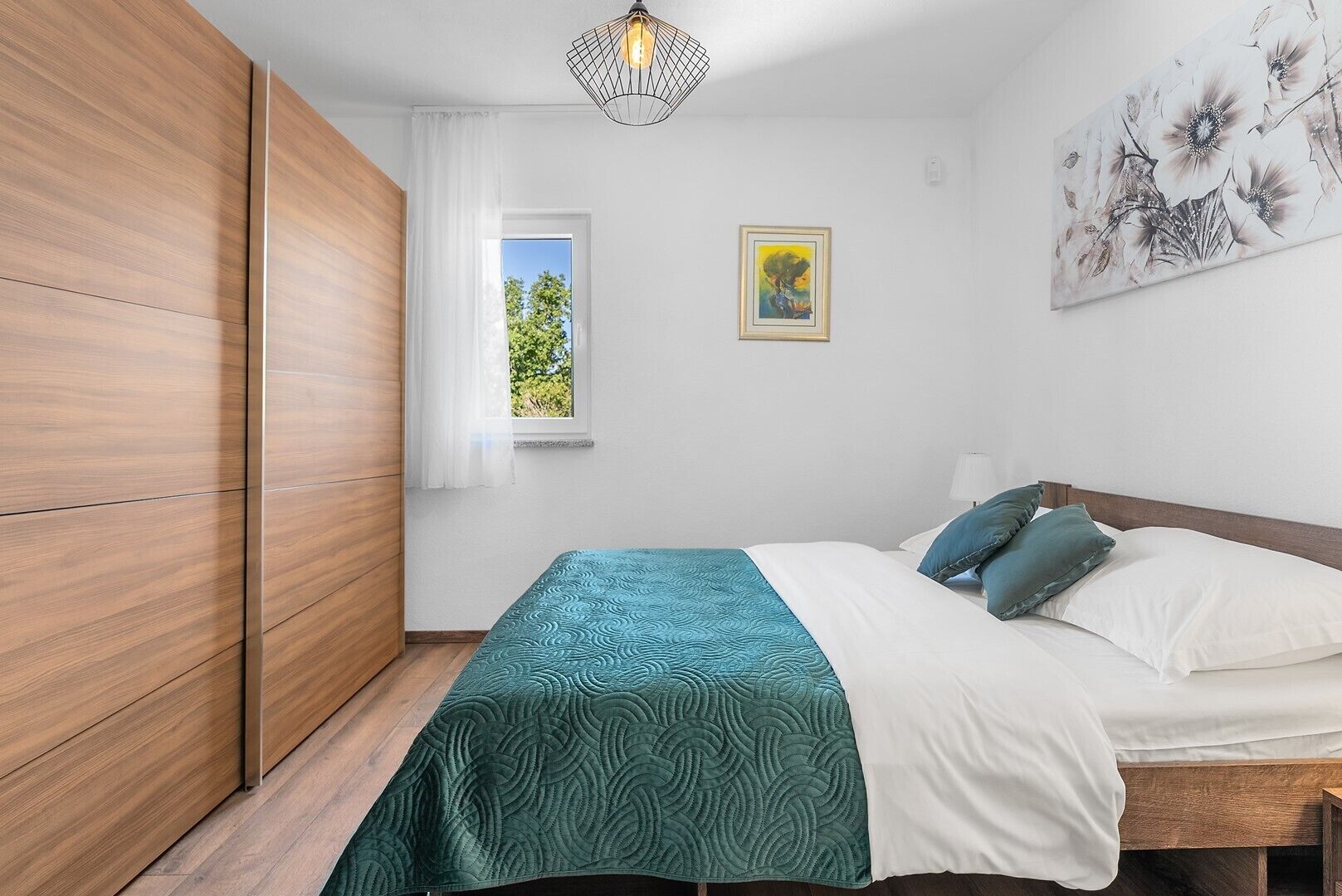 A bedroom with a bed, a window, a painting, and a wardrobe.