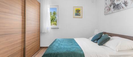 A bedroom with a bed, a window, a painting, and a wardrobe.