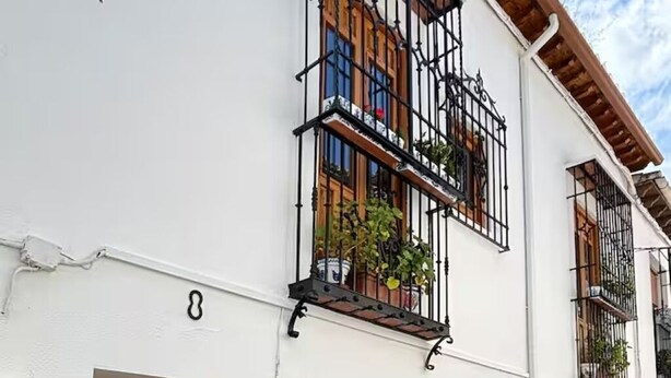 Een wit gebouw met een houten deur, nummer 8, en meerdere balkons met metalen leuningen en plantenbakken.