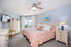 Une chambre à coucher comprenant un lit, un bureau, une chaise, une armoire, une table de chevet, une lampe, un ventilateur de plafond et une fenêtre avec des rideaux.