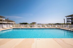 Une piscine rectangulaire entourée d’une clôture blanche, avec des chaises longues et un kiosque en arrière-plan.