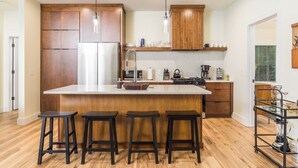 Une cuisine moderne avec des meubles en bois, un îlot central doté de tabourets et une machine à café.