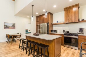 Cozinha moderna com armários de madeira, ilha central com banquetas, eletrodomésticos de aço inoxidável e iluminação pendente.