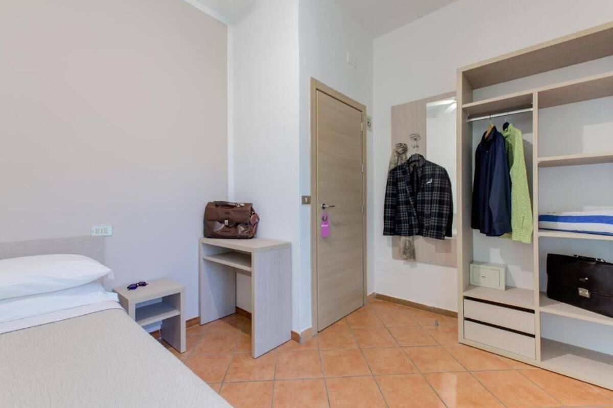 Quarto com cama, uma escrivaninha pequena, guarda-roupa e porta.
