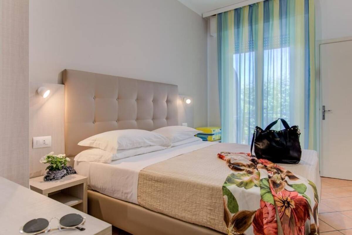 Quarto de hotel com cama, mesa de cabeceira e janela com cortinas.