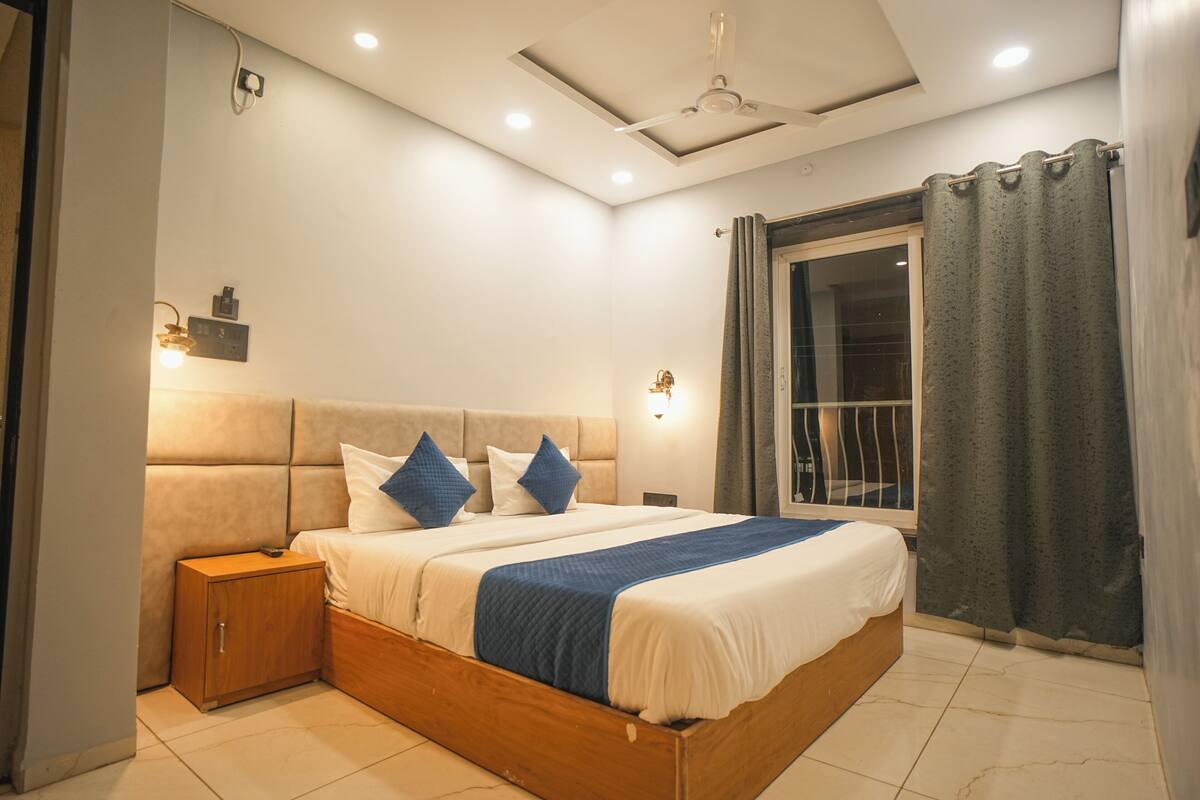 Une chambre à coucher avec un grand lit, une table de chevet, un ventilateur de plafond et une fenêtre avec des rideaux.