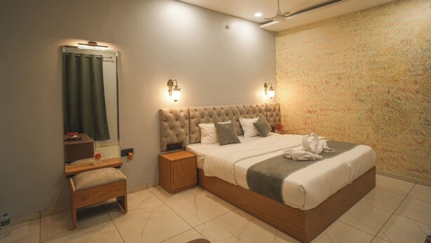 A bedroom with a large bed, a nightstand, a wooden bench, a mirror, and a ceiling fan. - Bhopal Inn by Ten On Ten Stays (Bhopal)
