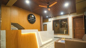 A hotel reception area with a wooden reception desk, a large window, and a ceiling fan. - Bhopal Inn by Ten On Ten Stays (Bhopal)