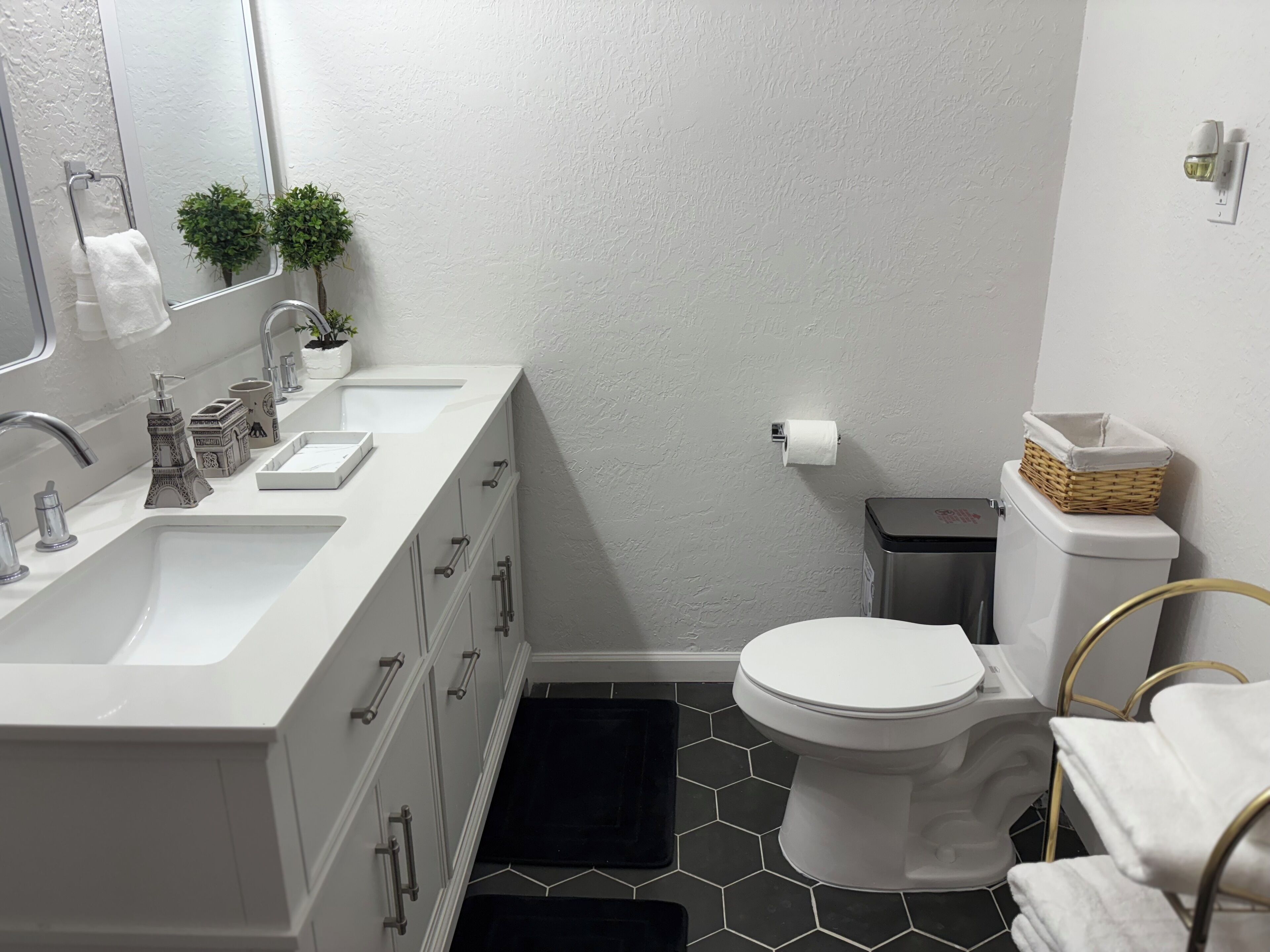 Une salle de bain moderne avec un meuble-lavabo blanc, des toilettes et un sol noir à motifs hexagonaux.