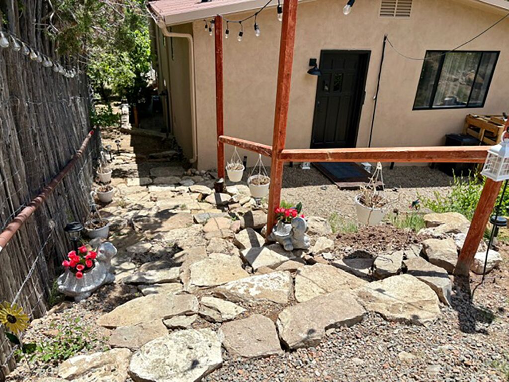 A stone-paved courtyard with a wooden bench, potted plants, and a rustic fence.