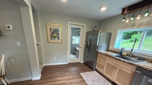 A kitchen with wooden flooring, a refrigerator, a sink, and a window with a view of greenery. - Newly remodeled cozy 3BR/1BA home on a hill, minutes from town. (Hancock)
