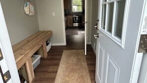 A hallway with a wooden bench, a rug, and a door leading to a kitchen. - Newly remodeled cozy 3BR/1BA home on a hill, minutes from town. (Hancock)