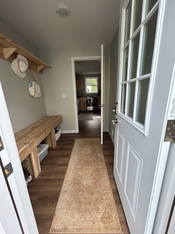 Un pasillo con un banco de madera, una alfombra y una puerta que da a una cocina.