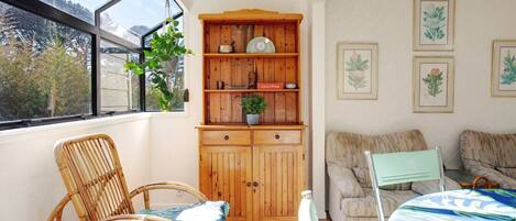 A cozy room with a wooden cabinet, wicker chairs, a sofa, and framed botanical prints on the wall.