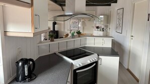 Une cuisine de taille réduite avec des meubles blancs, un plan de travail noir, une cuisinière et une bouilloire.