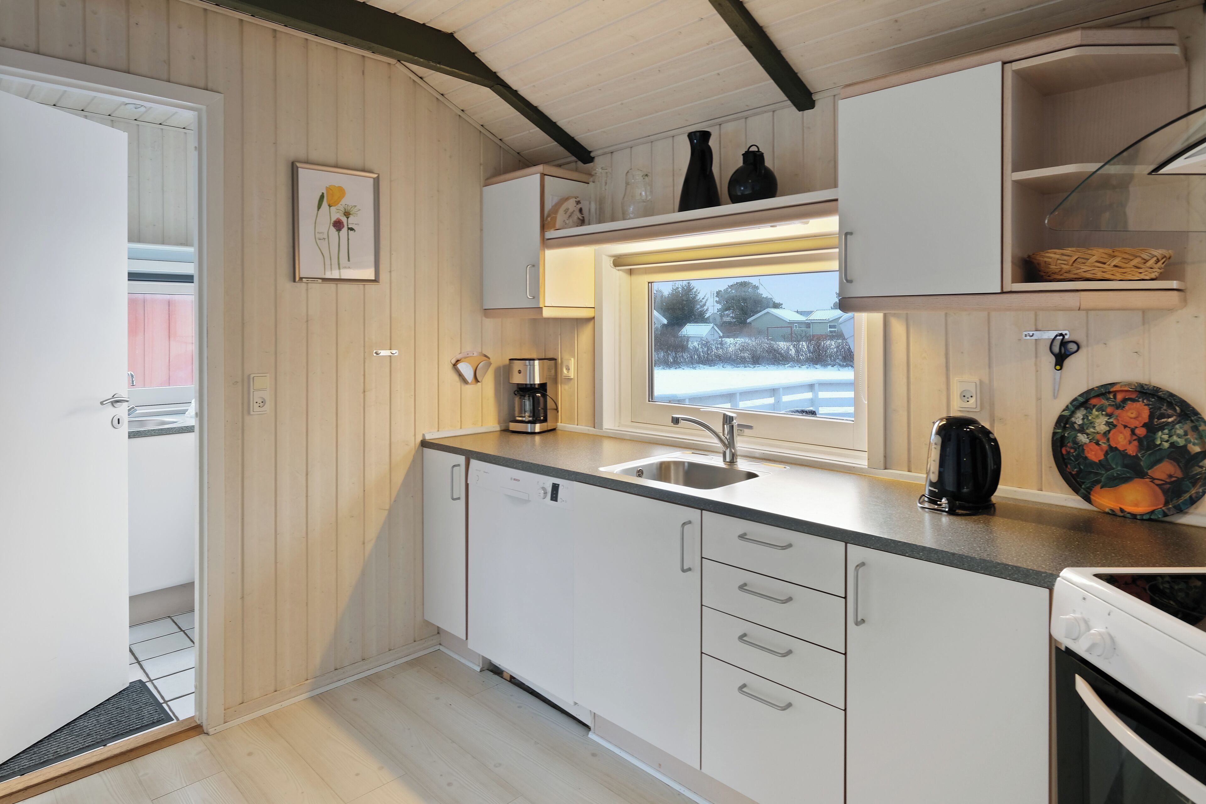 A compact kitchen with white cabinets, a built-in oven, a coffee maker, and a window with a view of the outside.