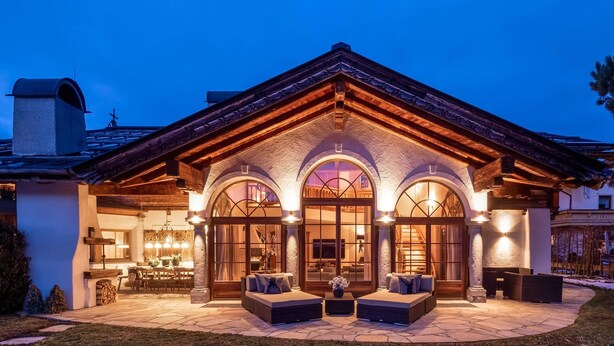 A large, modern house with a stone facade, arched windows, and a spacious patio area with outdoor seating.