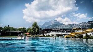 A swimming pool with people, a water slide, and mountains in the background.