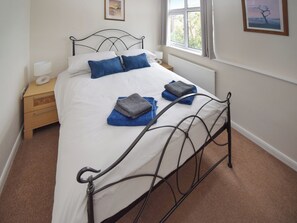 A neatly made bed with blue and grey towels, a bedside table with a lamp, and a window with curtains.