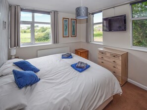A bedroom with a bed, a dresser, a radiator, and a TV. - A Perfect Escape for Train Enthusiasts. (St Bees)