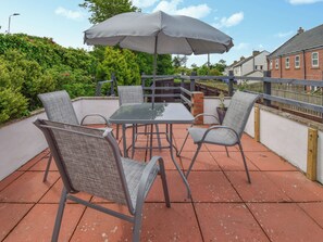 An outdoor patio with a table and four chairs, an umbrella, and a view of a brick house and greenery. - A Perfect Escape for Train Enthusiasts. (St Bees)