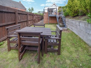 A wooden picnic table and benches in a backyard with a brick wall and a wooden fence. - A Perfect Escape for Train Enthusiasts. (St Bees)