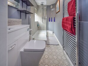 A compact bathroom with a toilet, sink, shower, and a towel rack with a red towel. - A Perfect Escape for Train Enthusiasts. (St Bees)