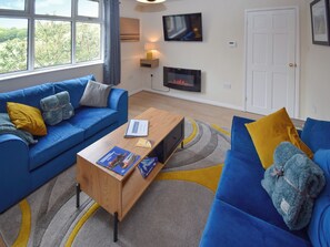 A modern living room with a blue sofa, a wooden coffee table, and a flat-screen TV mounted on the wall.