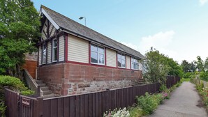 Une maison à deux étages, avec une base en briques et un niveau supérieur blanc, dotée d’un petit porche à l’avant et d’une clôture en bois.